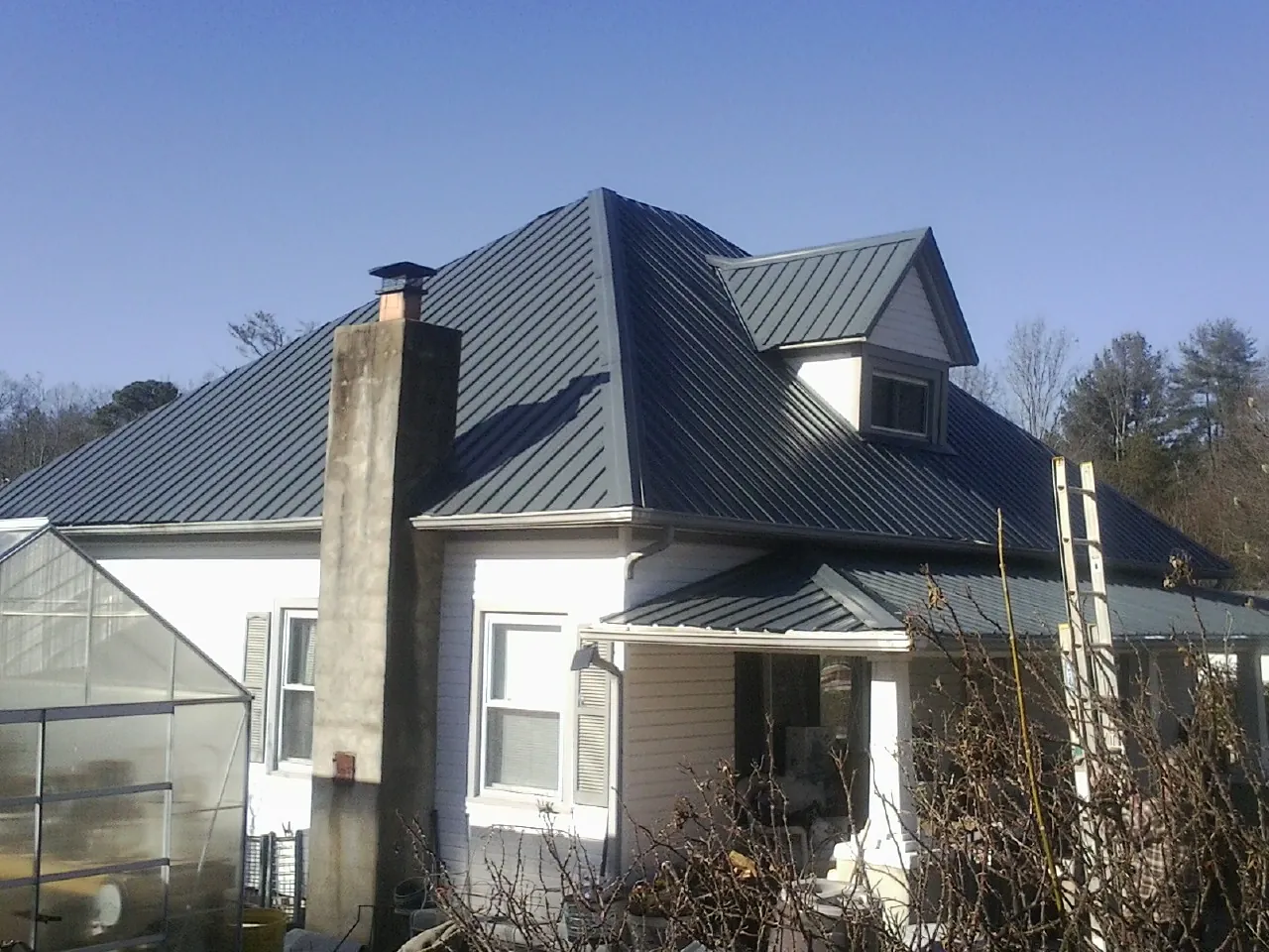 Dark blue standing seam metal roof on a white farmhouse with dormer — Slate & Tile Roof Repair by Roofing Brothers in Warrensburg