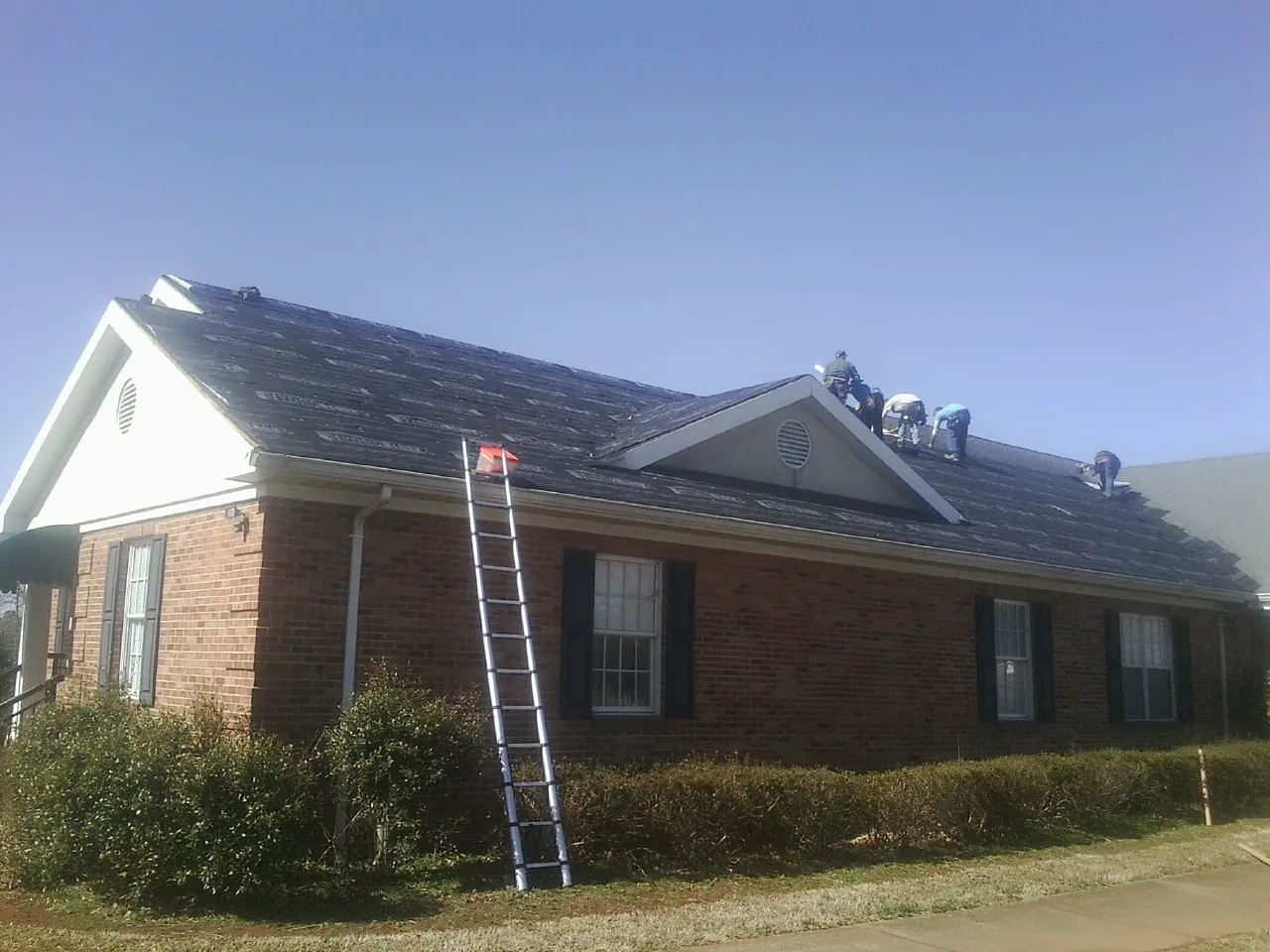 Crew tearing shingles off a brick ranch roof with a ladder set — Emergency Roof Repair work by our crew in Warrensburg