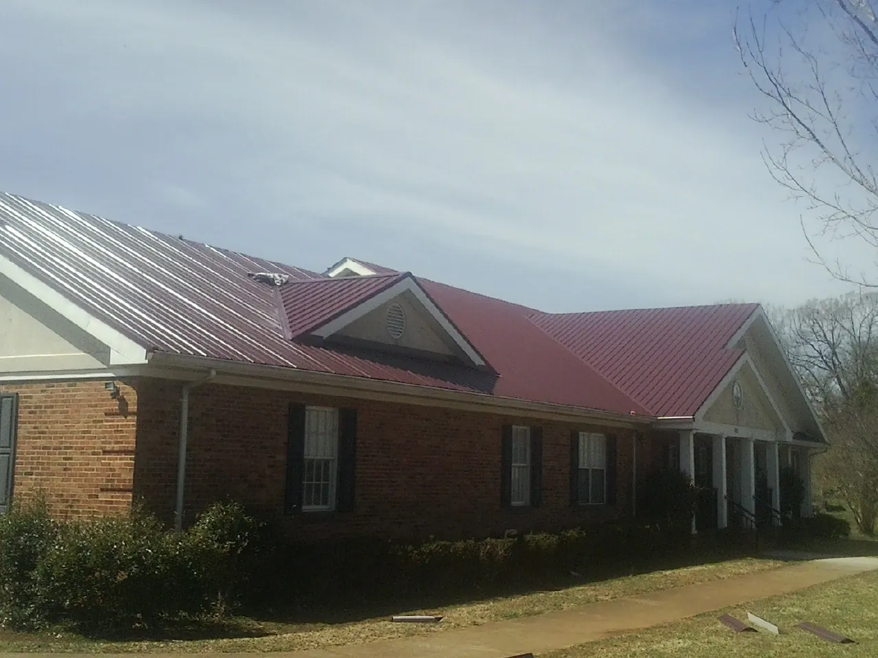 Red metal roof with gabled entries on a long brick building, from a Hail Damage Roof Repair job in Warrensburg