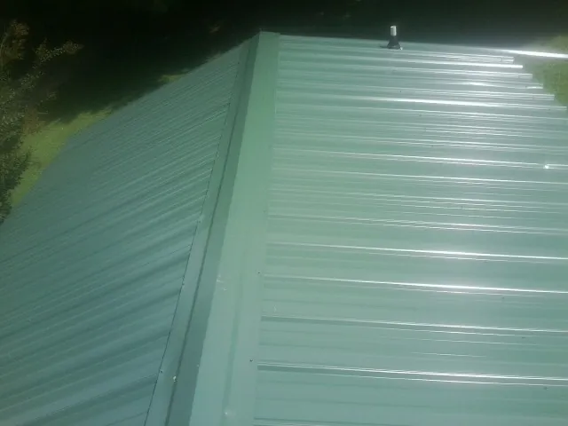 New green metal panels meeting at the ridge of a roof — Flat Roof Repair work by our crew in Warrensburg