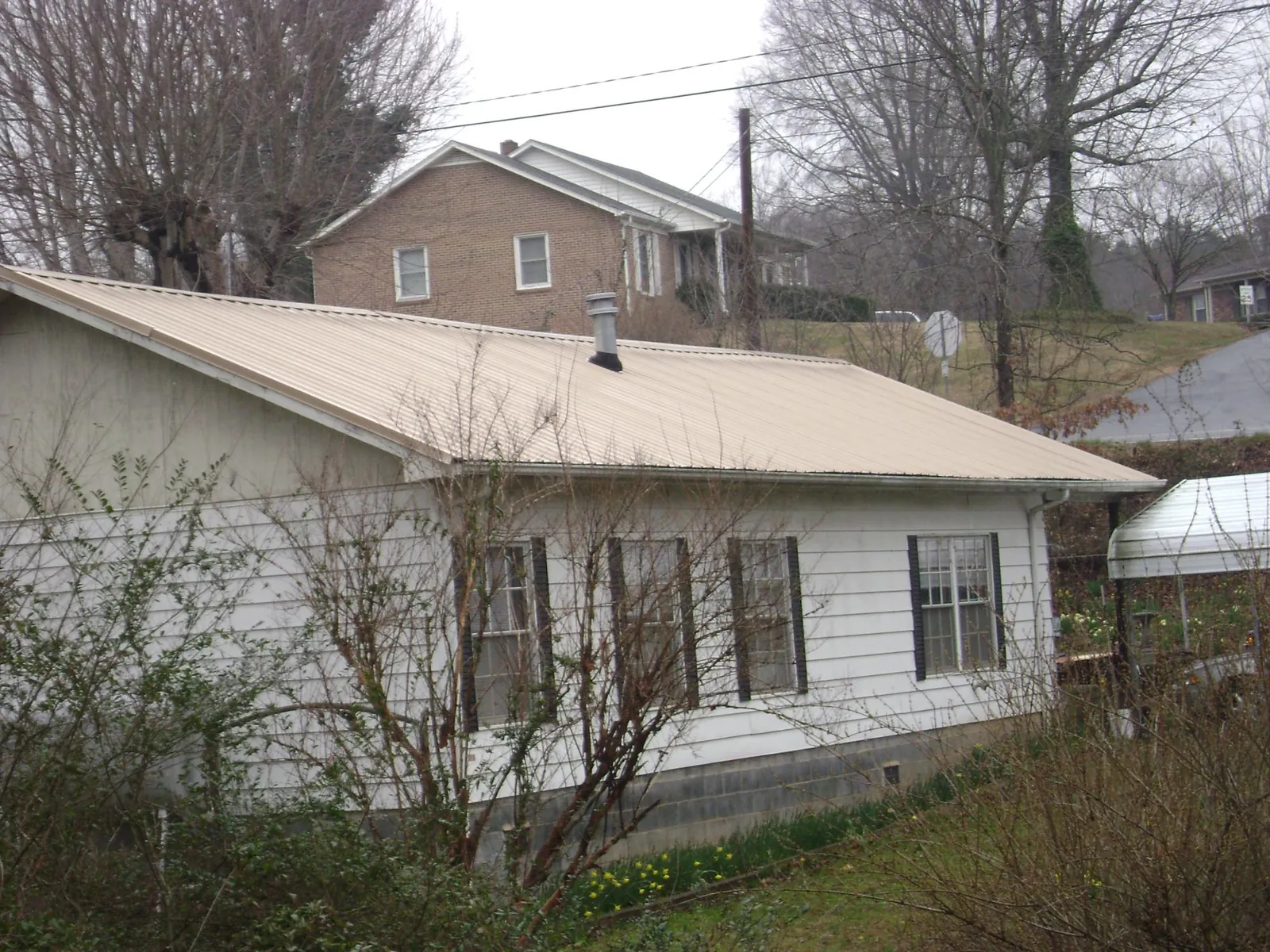 Tan metal roof on a white sided house set into a hillside — Commercial Roofing by Roofing Brothers in Warrensburg