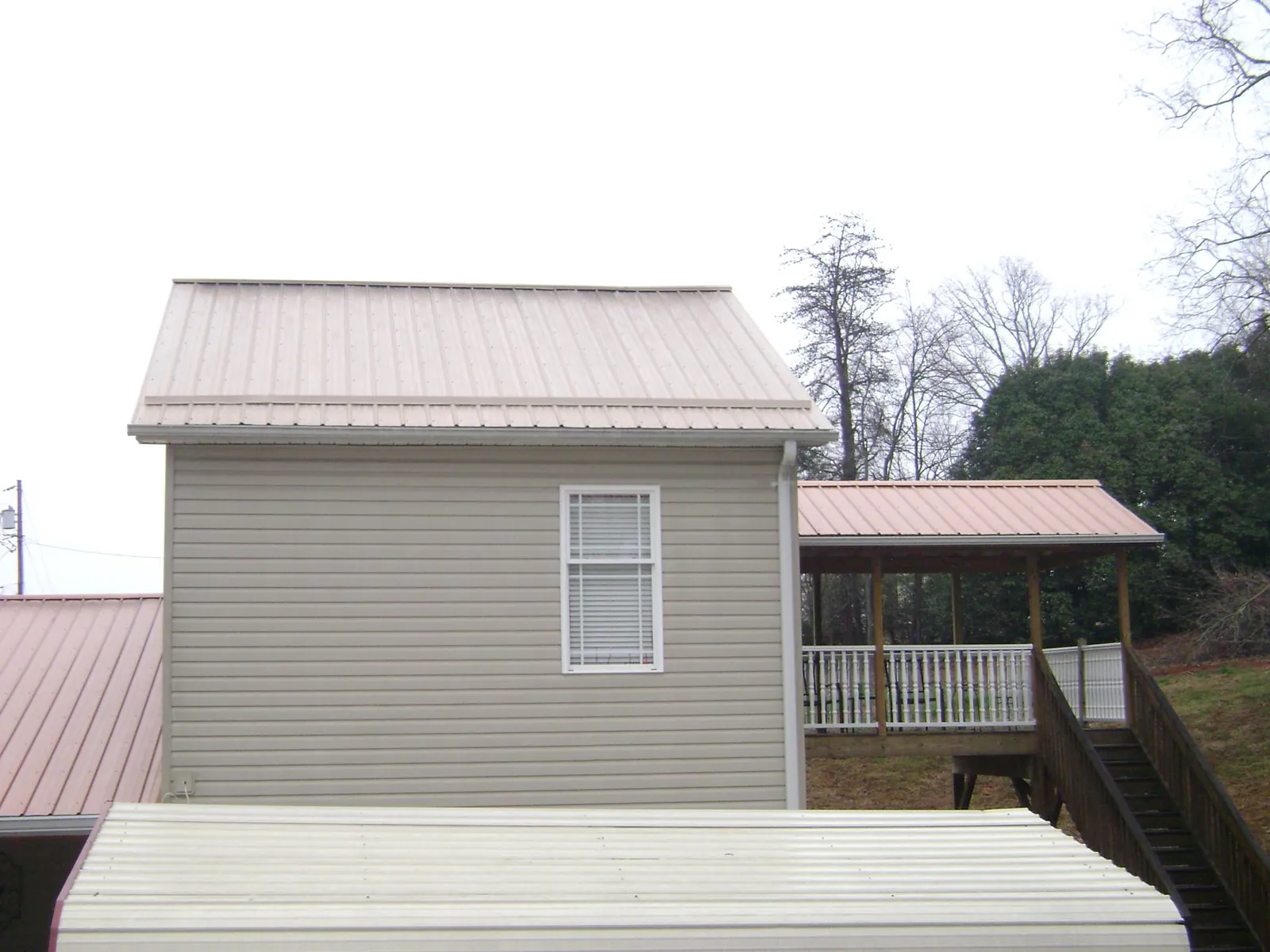 Tan metal roofs on a two story addition and attached porch, from a Roof Replacement job in Warrensburg